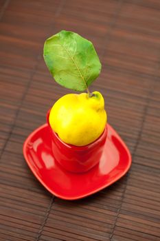 yellow quinces with green leaves in a cup on a bamboo mat