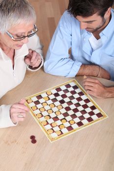 Senior woman playing checkers with a young man