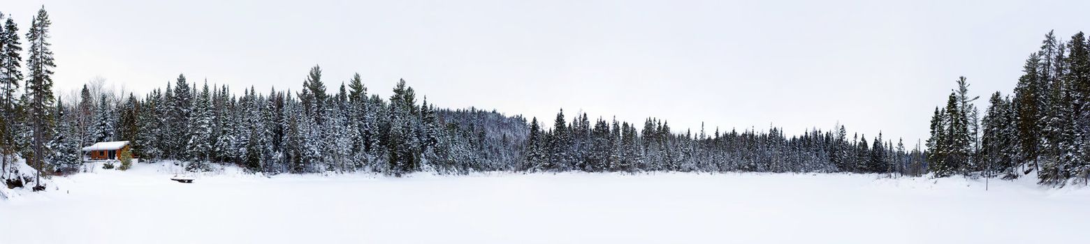 Panorama of frozen lake with log cabin