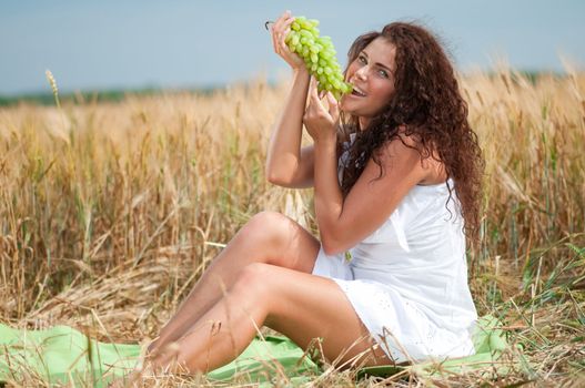 perfect woman eating grapes in wheat field. Picnic.