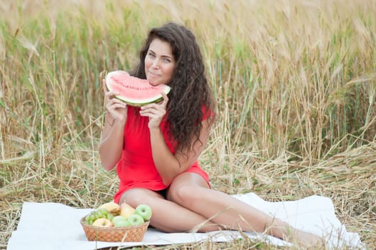 Woman in wheat field eating watermelon. Picnic.