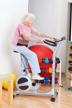 Full length of senior woman exercising on bike in gym