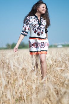 Beautiful woman walk in wheat field on sunny summer day.