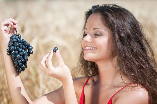Nice woman in wheat field eating grapes.