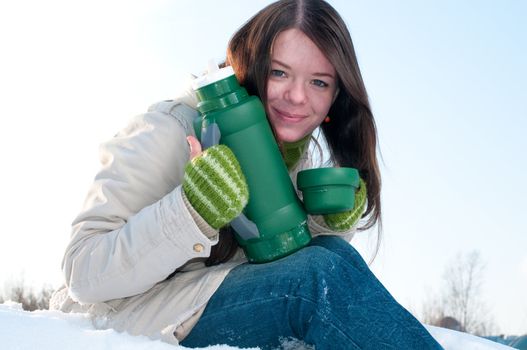 Girl on winter picnic with cup of hot tee and thermos