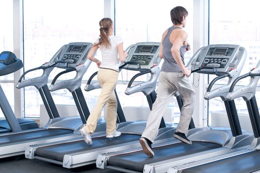 Young woman and man at the gym exercising. Run on on a machine.