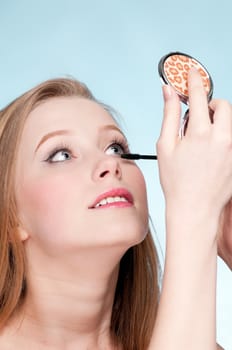 Beautiful young adult woman applying cosmetic mascara brush