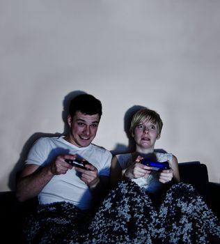 Young couple playing video games comfortably wrapped in a blanke