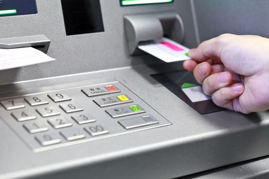 Hand inserting ATM credit card into bank machine to withdraw mon