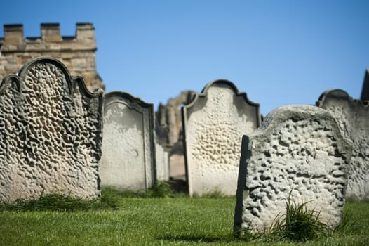 Old weathered gravestones arranged haphazardly on green grass, closeup view against a blue sky