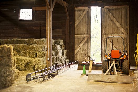 Interior of wooden barn with hay bales stacks and farm equipment