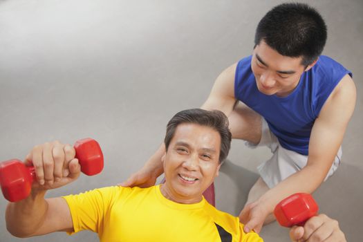 Mature man working out with weights, trainer supporting him 