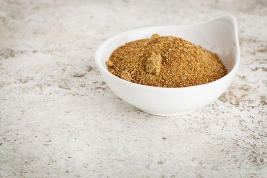 small ceramic bowl of unrefined coconut palm sugar against a ceramic tile background with a copy space