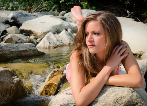 Pretty brunette girl in bikini laying on rocks by small water stream