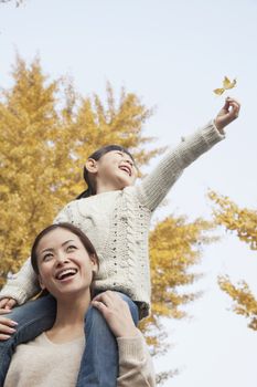 Daughter Riding Piggy-Back on Mother's Shoulders Enjoying Autumn Leaves