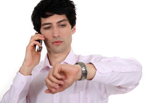 Businessman looking at his watch while taking a call