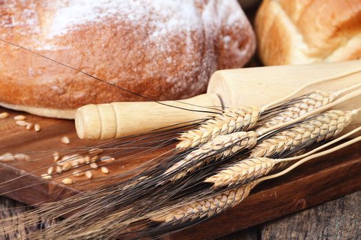 Heads of wheat with a variety of freshly baked breads and rolling pin against a rustic background.