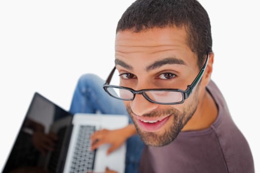 Man wearing glasses sitting on floor using laptop and smiling up