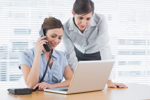 Businesswoman calling and looking at laptop with colleague