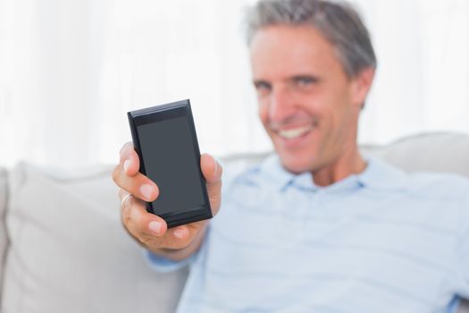 Man showing smartphone to camera at home on couch