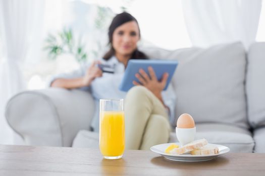 Peaceful brunette having breakfast while buying online in her living room