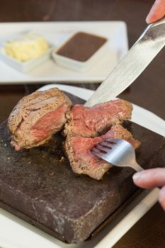 Medium rare steak sizzling on hot stone plate being sliced