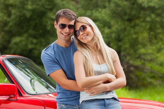 Cheerful couple hugging and leaning against cabriolet