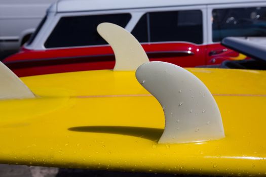 Yellow surfboard keel fins detail eith red retro car in Califor