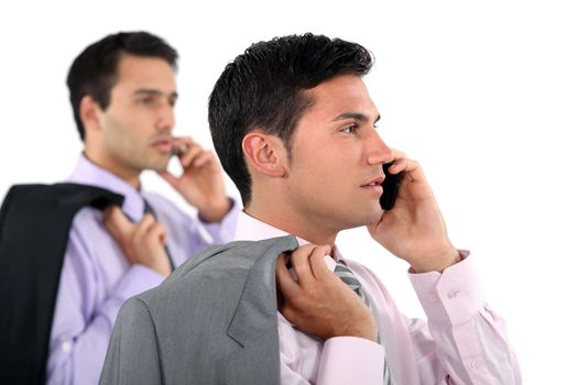 Two businessmen with jackets over shoulders making phone calls