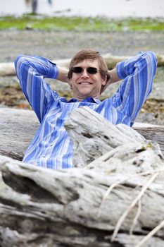Man in forties leaning back against log on beach