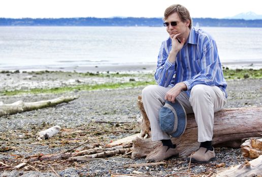 Depressed man sitting on driftwood on beach