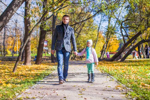 Adorable little girl with happy father walking in autumn park on a sunny day
