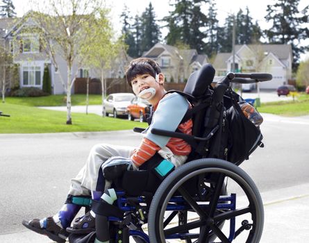 Happy disabled six year old boy waiting on sidewalk in wheelchai
