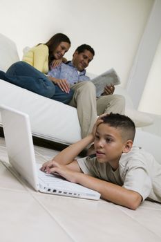 Boy Using Laptop on Floor in living room mother and father on sofa ground view