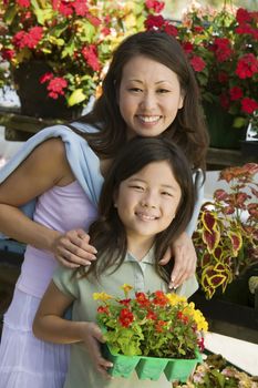 Mother with daughter holding young flowers in plant nursery portrait