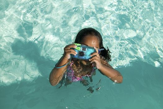 Girl (5-6) Using Waterproof Camera in Swimming Pool overhead view.