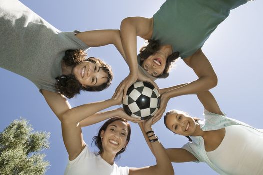 Girl with friends and mother holding soccer ball together in a huddle