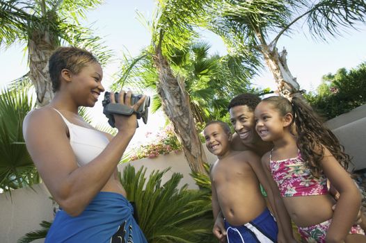 Mother Videotaping Family in swim wear in back yard side view