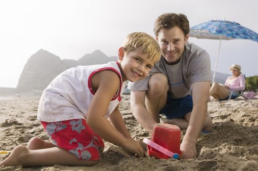 Father building sandcastle with son on beach