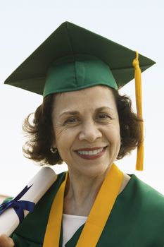Portrait of a happy senior woman in graduation robe holding degree