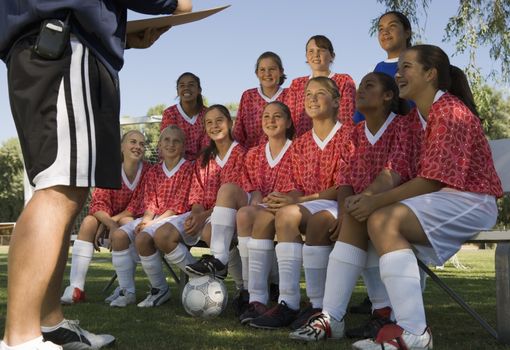 Group of multiracial female soccer players listening to coach on field