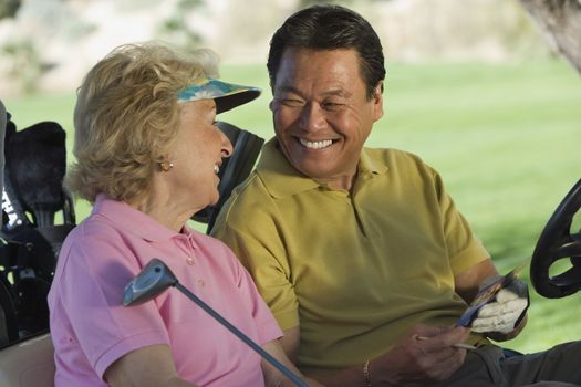 Happy man and woman with scorecard sitting in golf cart