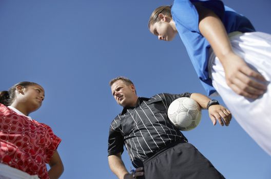 Rival female soccer players standing in front of referee against sky