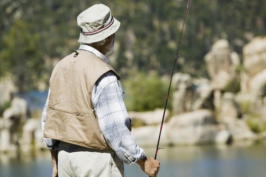 Rear view of Hispanic senior man standing with a fishing rod
