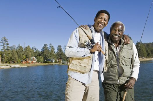 Portrait of happy senior man and adult son holding fishing rods by lake