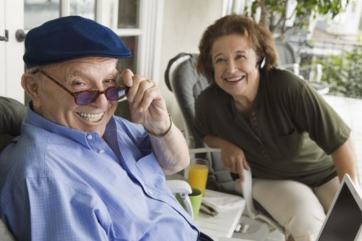 Cheerful senior man holding sunglasses with woman in background