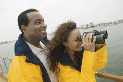 Happy African American woman with man on yacht looking through binoculars