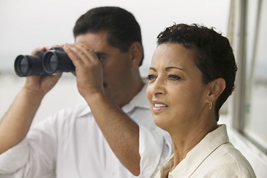 Mature man looking through binoculars with woman standing besides on the yacht