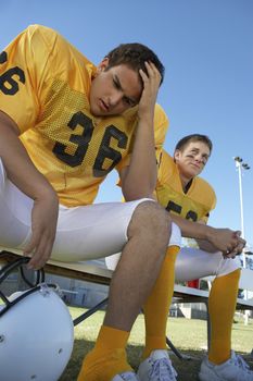 Low angle view of a tense rugby player sitting with teammate on bench