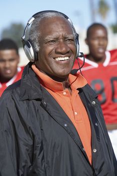 Happy senior African American coach wearing headphones with players in background